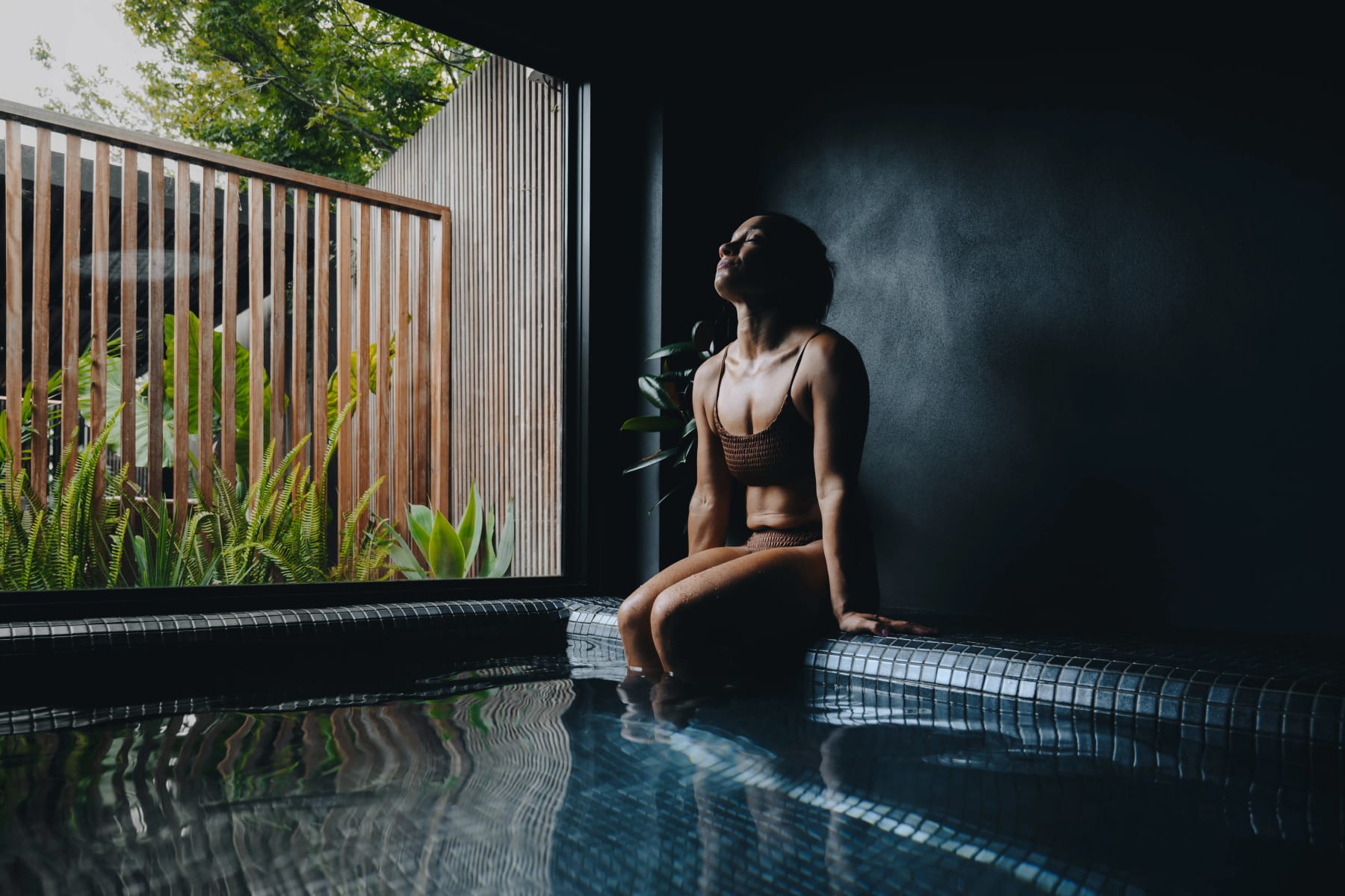 A bather resting on the edge of the mineral pool beside the garden window
