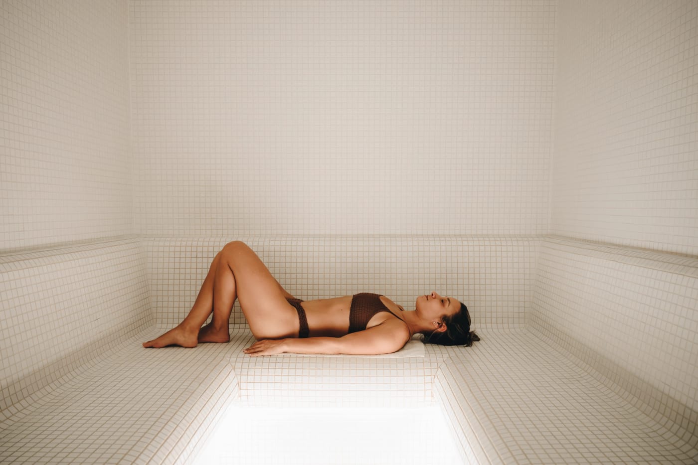 A bather lying on the bench in the white tiled steam room