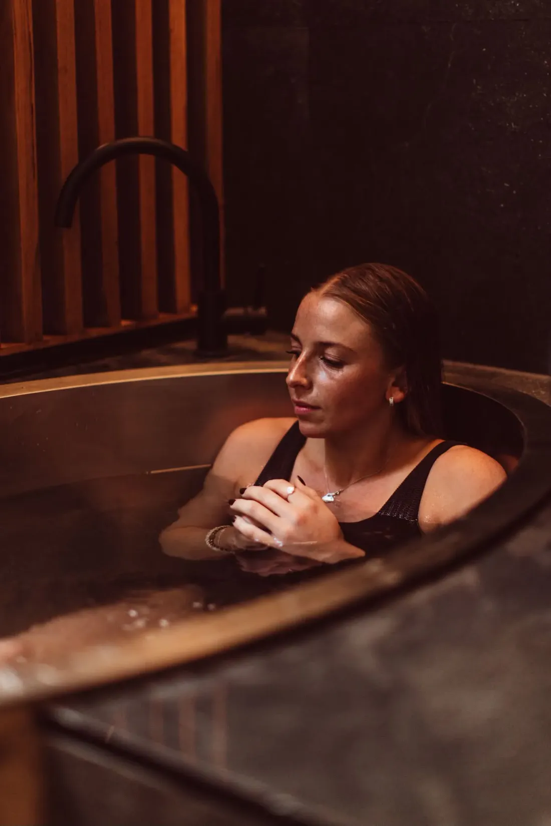 A guest resting in a timber barrel bath in warm light