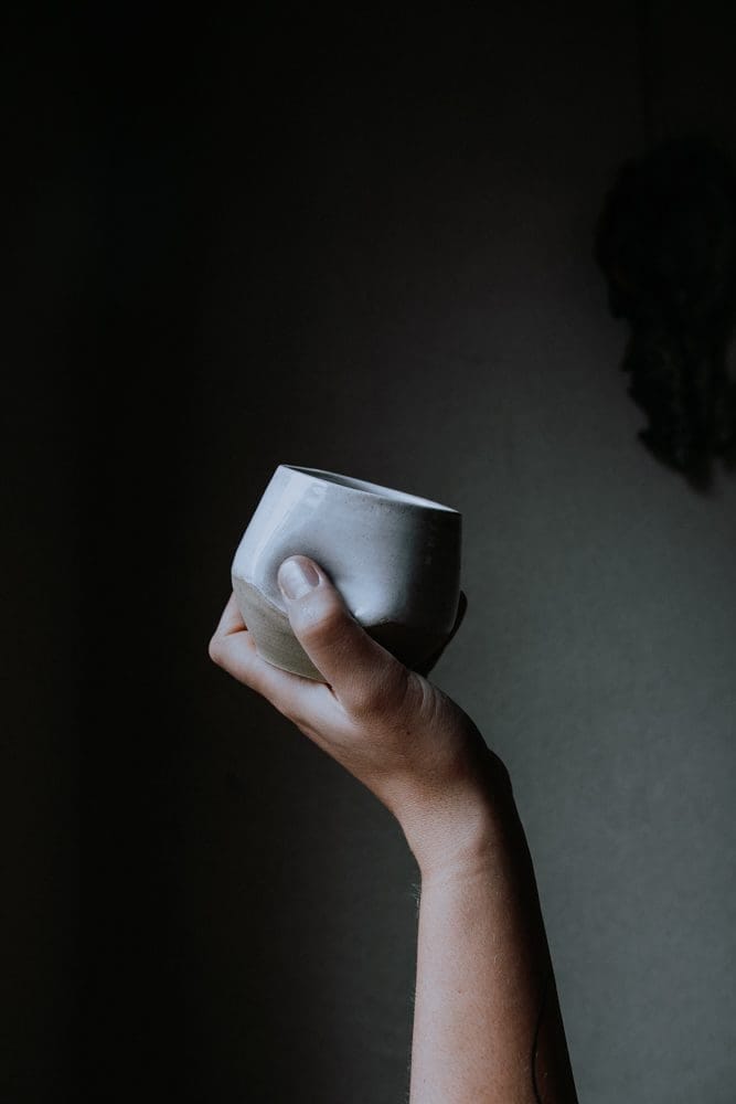 A hand raising a pale handmade ceramic cup