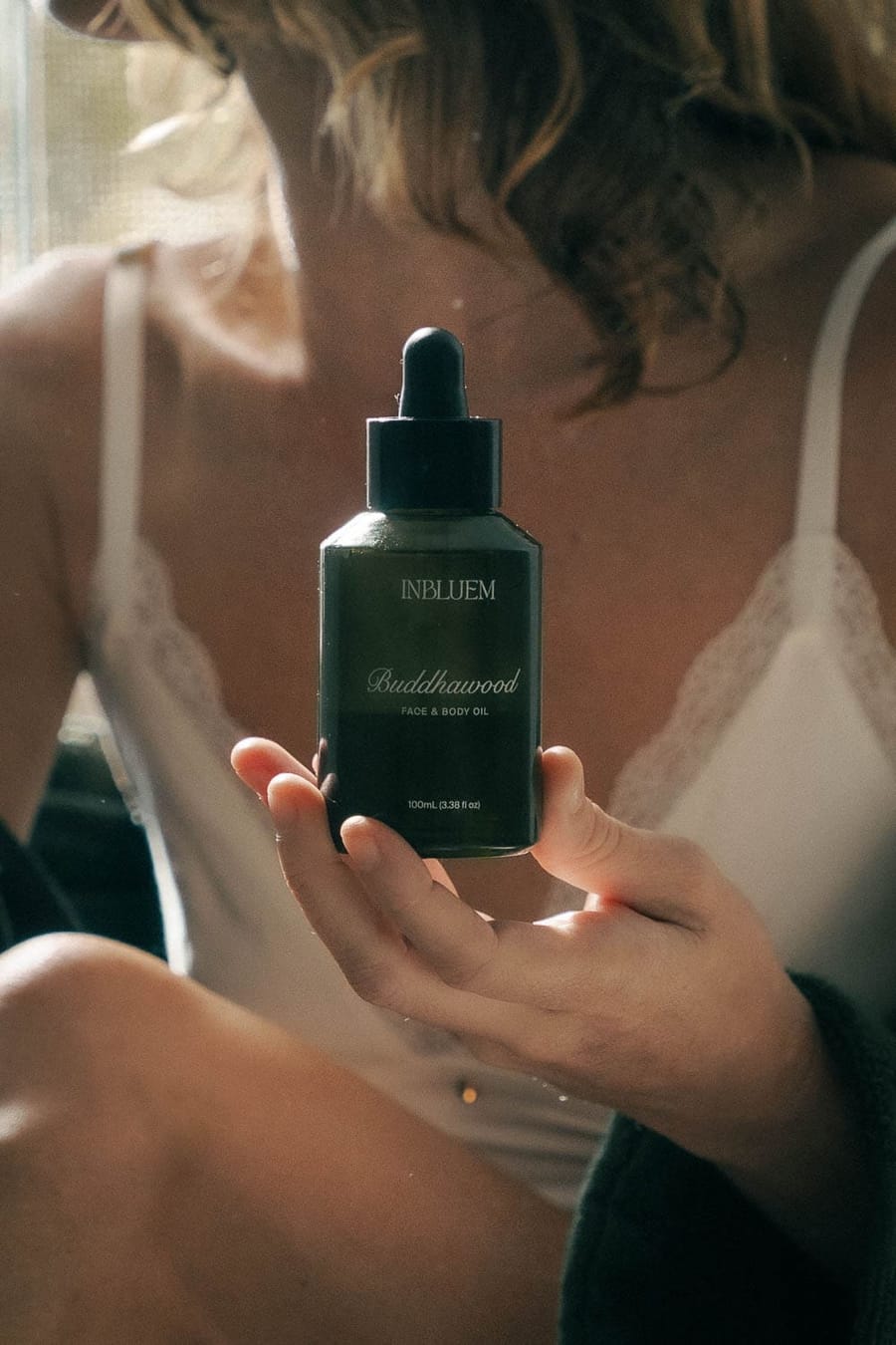 A hand holding a dark glass bottle of INBLUEM oil