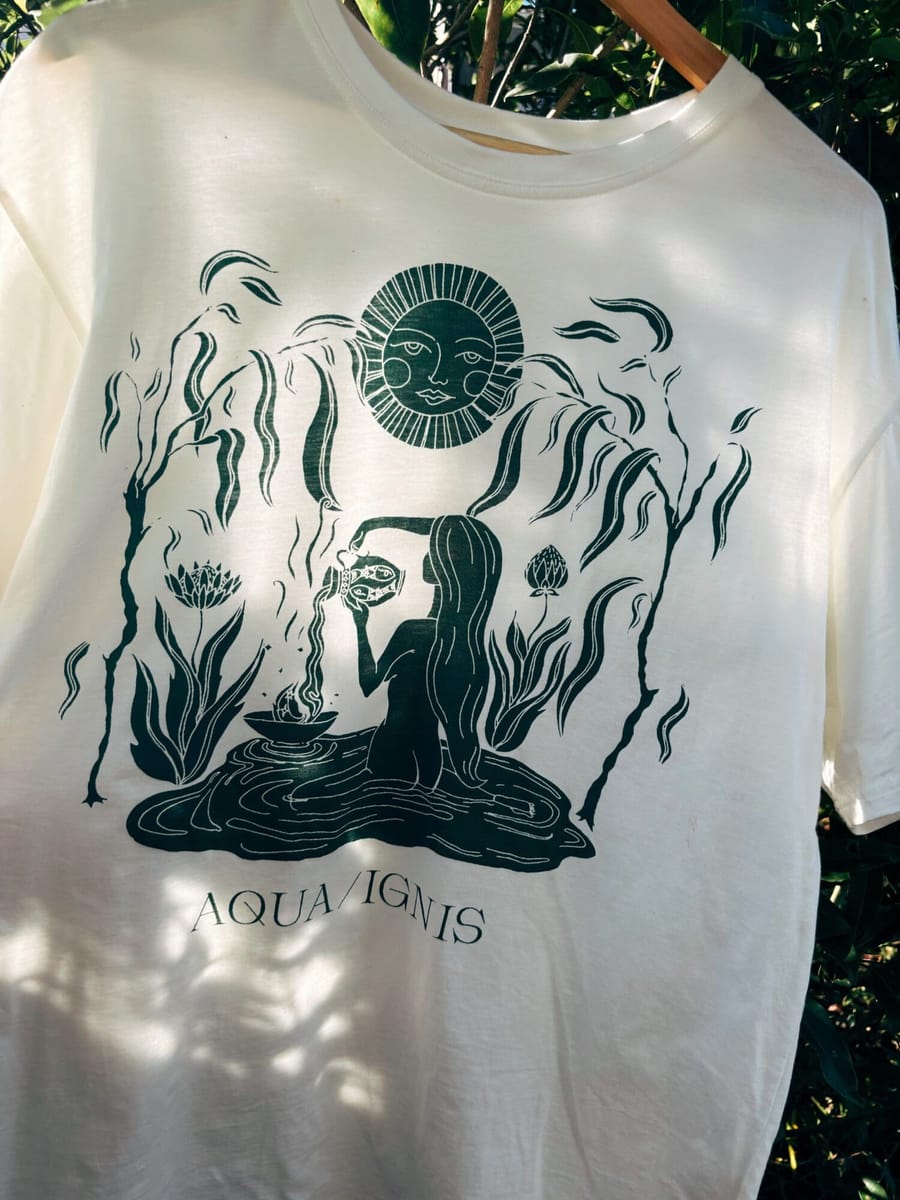 A cream Aqua Ignis tee with a green print of a bather, sun and plants